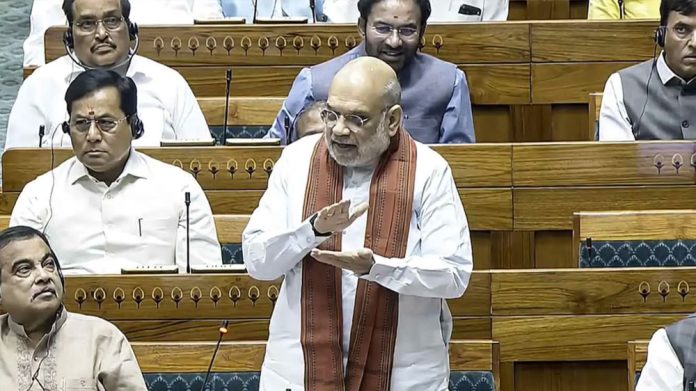 Prime Minister Narendra Modi speaks in a parliamentary chamber, gesturing with his hands as colleagues listen nearby.
